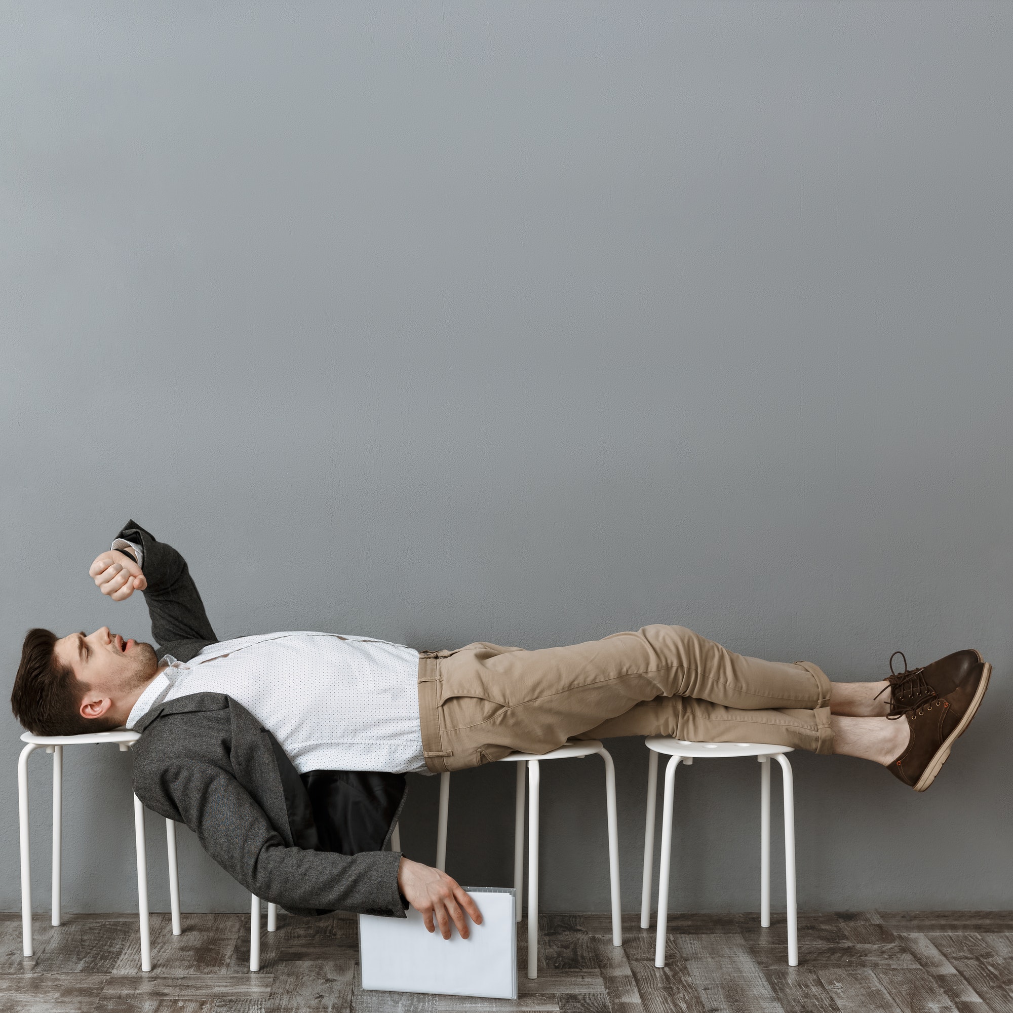 tired businessman with documents checking time while lying on chairs and waiting for job interview